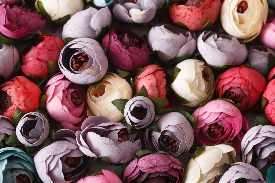 Dense arrangement of pink, purple, and cream peonies with dark centers and green leaves