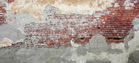 Weathered red brick wall with peeling white and grey plaster revealing aged texture layers