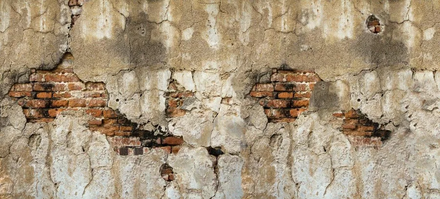 Weathered plaster wall with exposed red brick showing through cracks and deterioration.