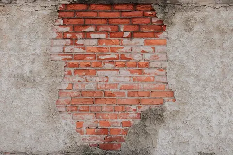 Weathered red brick wall with deteriorating cream plaster, showing authentic construction texture and aged patina.