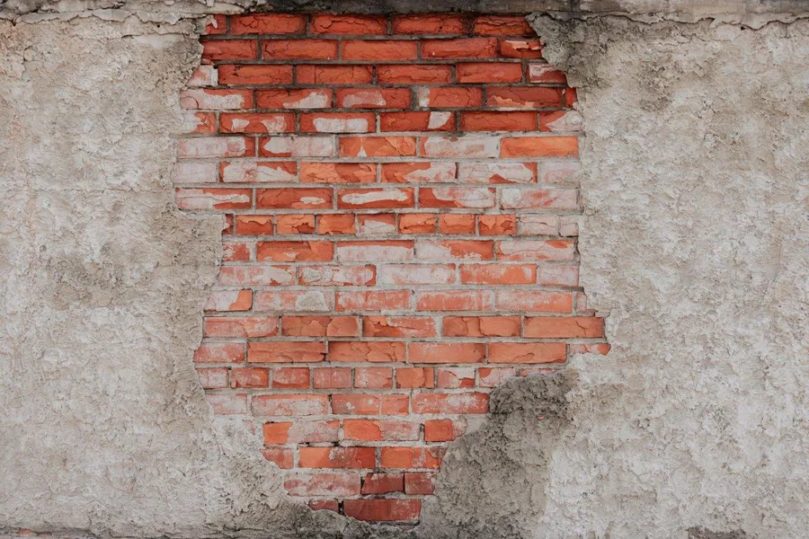 Weathered red brick wall with deteriorating cream plaster, showing authentic construction texture and aged patina.