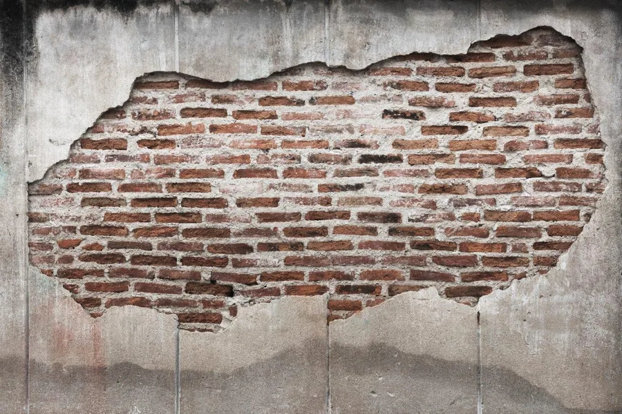Weathered exposed red brick wall with peeling grey plaster and realistic texture