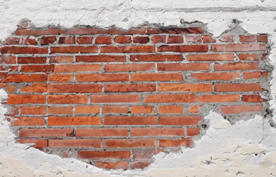 Weathered red brick wall with peeling white plaster and gray mortar joints