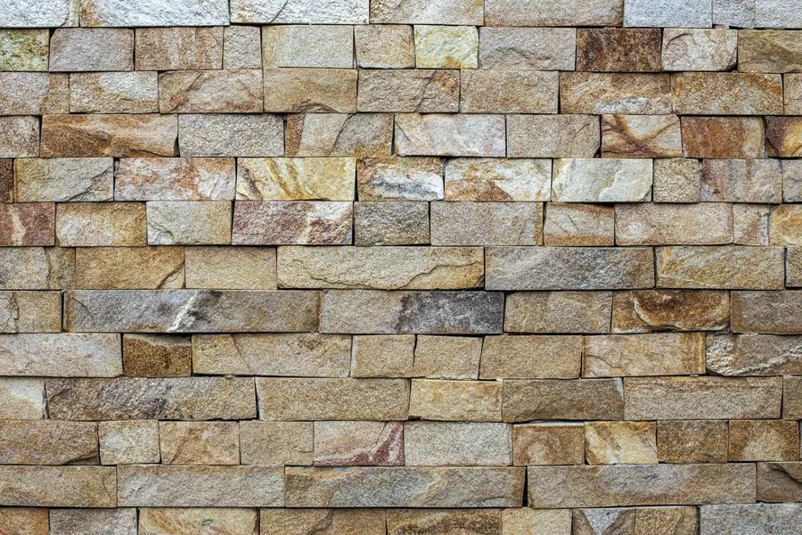 Repeating pattern of stacked rectangular bricks and stones in tan, brown, and grey tones with realistic shadows and texture.