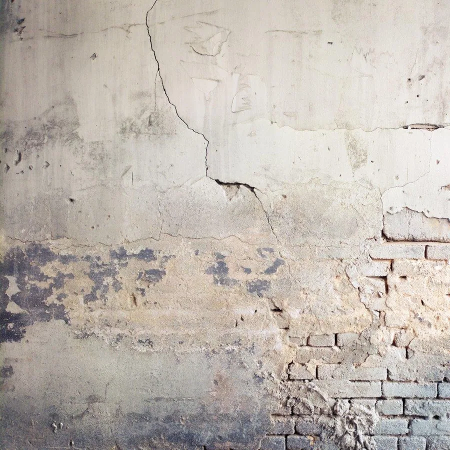 Cracked white plaster wall with exposed red brick showing natural weathering and decay patterns