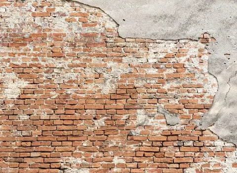 Weathered red brick wall with peeling grey plaster and aged mortar joints.