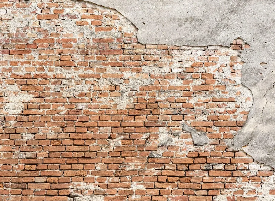 Weathered red brick wall with peeling grey plaster and aged mortar joints.
