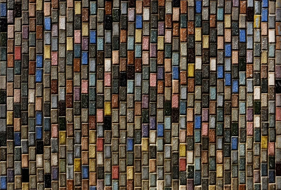 Multicolored weathered brick wall texture with varied earth tones, blues, and yellows in offset pattern