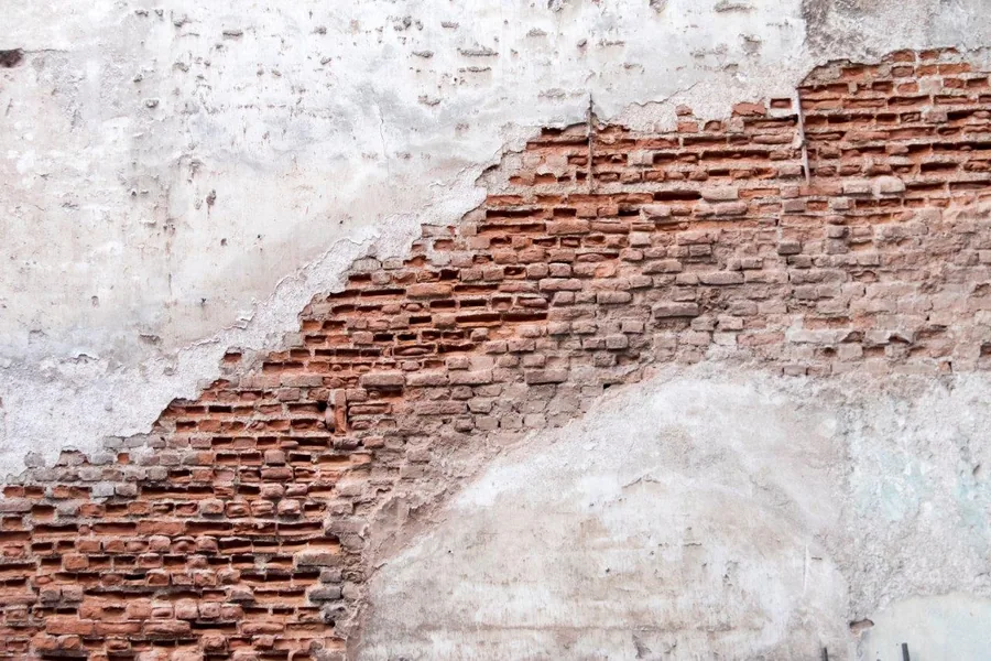 Peeling white plaster exposing red brick wall texture underneath
