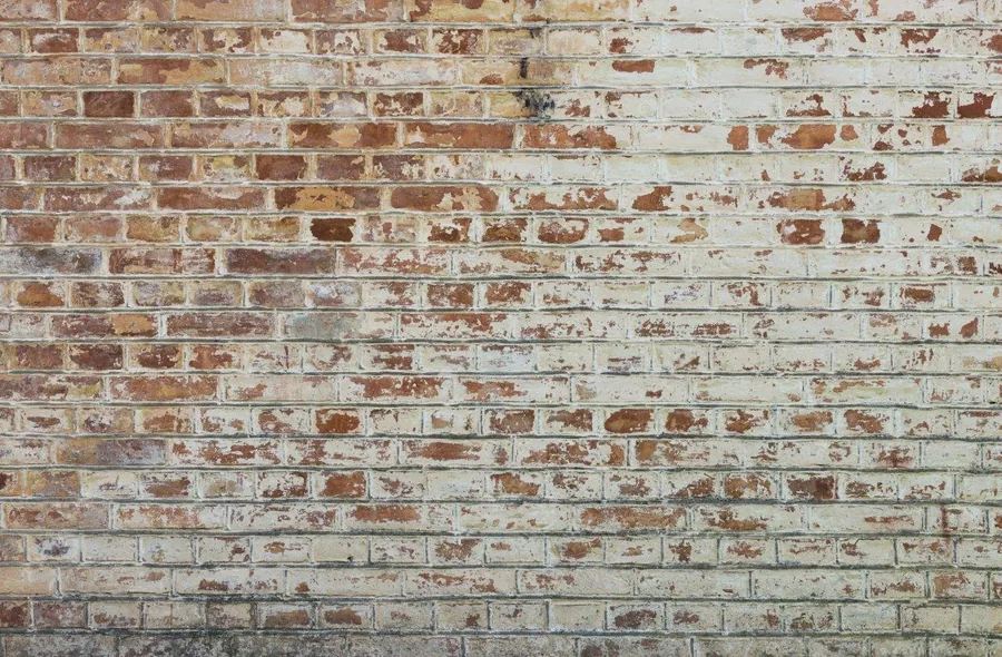 Peeling white painted brick wall with exposed red and cream bricks in weathered texture