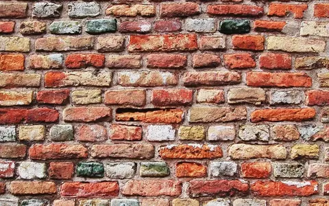 Close-up of aged brick wall with varied terracotta, cream, and grey bricks in running bond pattern