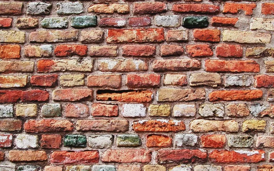 Close-up of aged brick wall with varied terracotta, cream, and grey bricks in running bond pattern