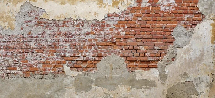 Aged brick wall with peeling cream and beige plaster revealing red brickwork beneath.