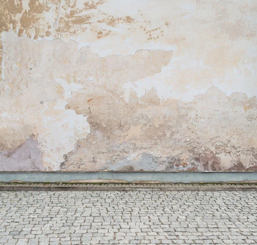 Weathered cream plaster wall with peeling paint and brick texture detail