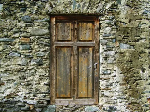 Weathered stone wall with distressed wooden four-panel door and moss-covered masonry