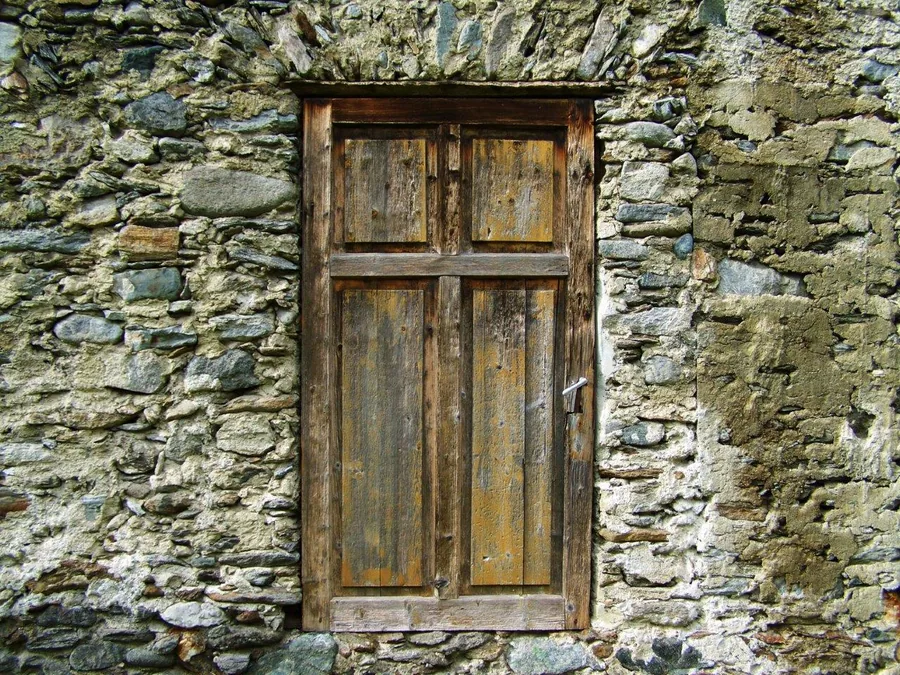 Weathered stone wall with distressed wooden four-panel door and moss-covered masonry