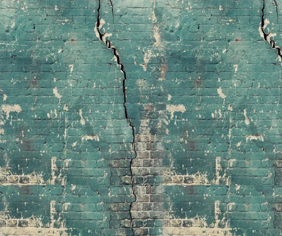 Aged turquoise painted brick wall with peeling paint and vertical crack running down center