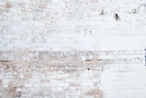 Weathered white and tan brick wall texture with peeling paint and aged patina