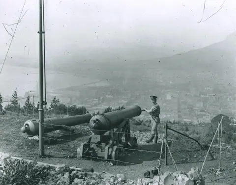 Black and white vintage photograph of a cannon on a hillside overlooking a foggy coastal city