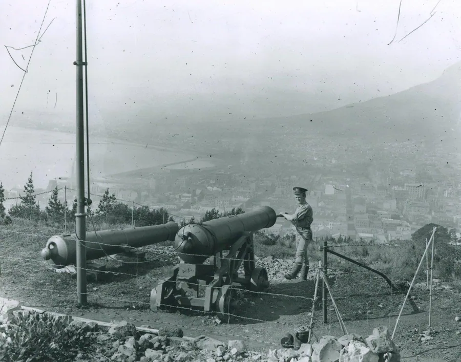 Black and white vintage photograph of a cannon on a hillside overlooking a foggy coastal city