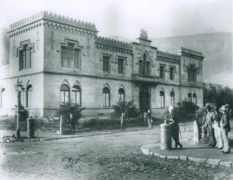 Historic black and white photograph of a colonial-era stone mansion with castellated roofline and arched windows