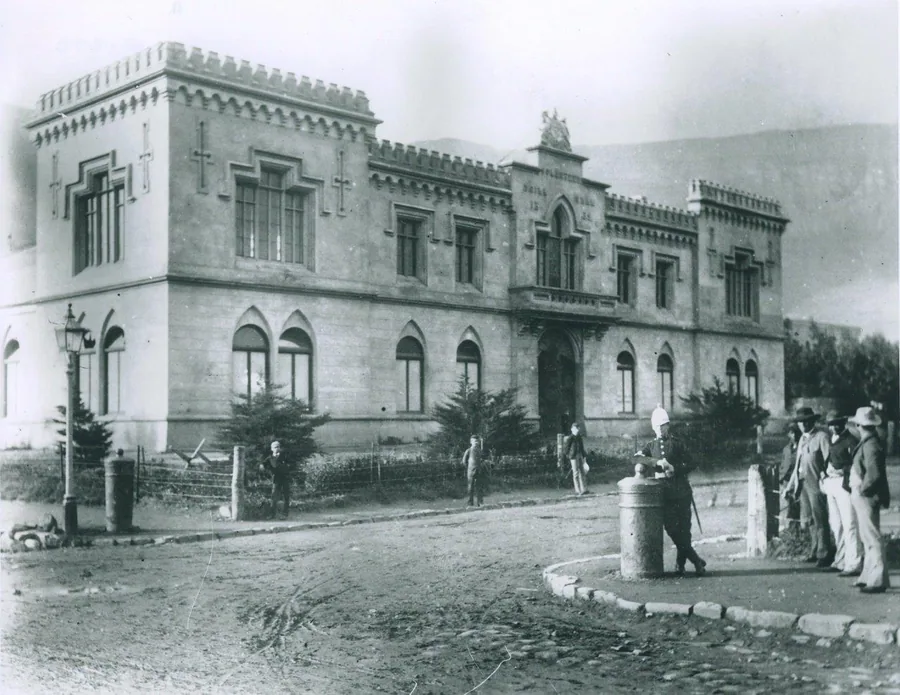 Historic black and white photograph of a colonial-era stone mansion with castellated roofline and arched windows