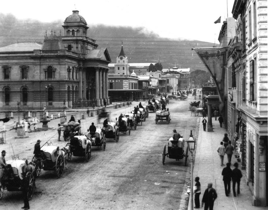 Historic black and white photograph of colonial-era Cape Town street with horse carriages and Victorian architecture