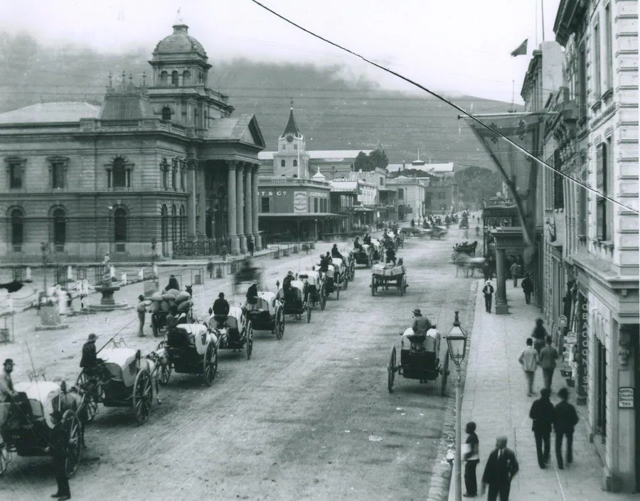 Vintage black and white photograph of a Cape Town street with colonial buildings, horse carriages, and pedestrians