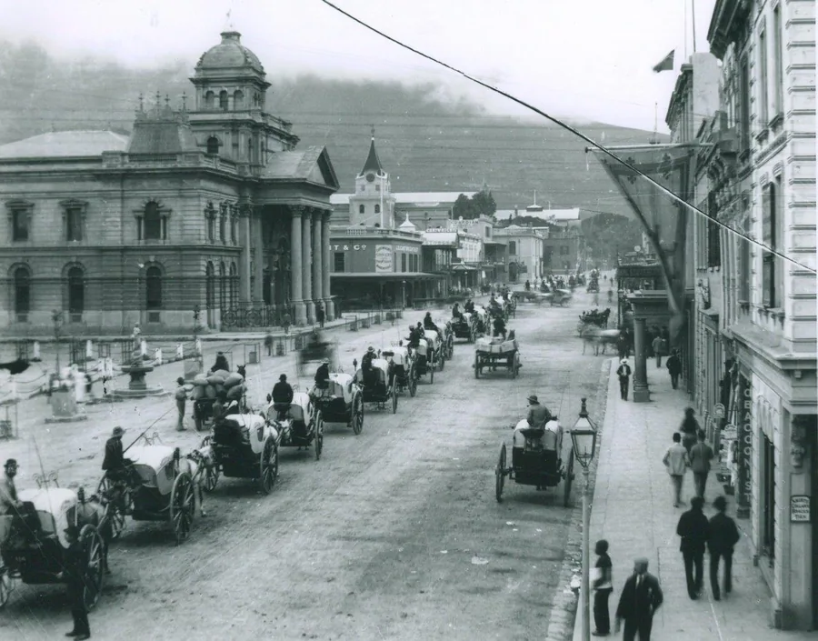Black and white vintage photograph of Cape Town street with colonial buildings, horse carriages, and Table Mountain in background