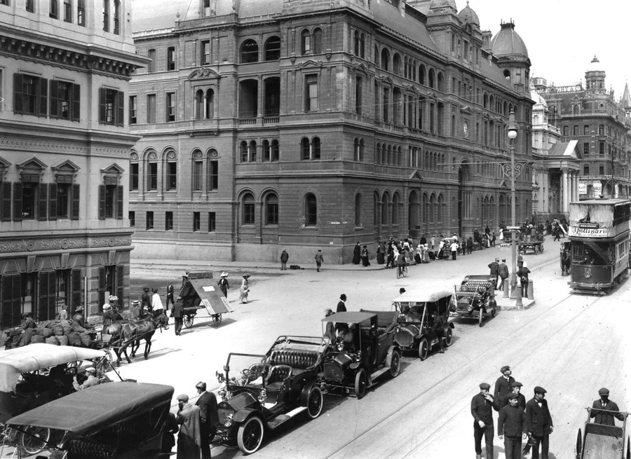 Black and white vintage photograph of classic cars and grand Victorian buildings on a historic city street