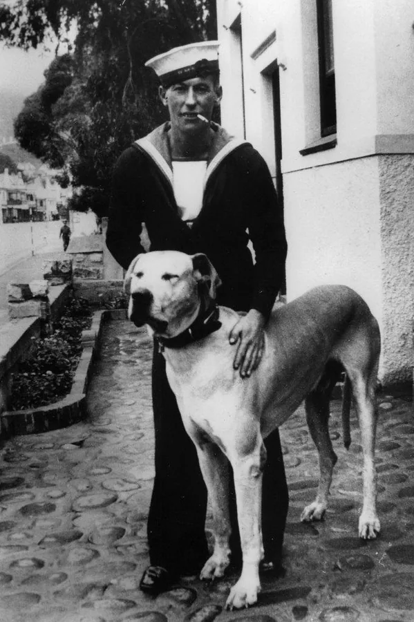 Black and white vintage photo of sailor in uniform with dog on cobblestone street