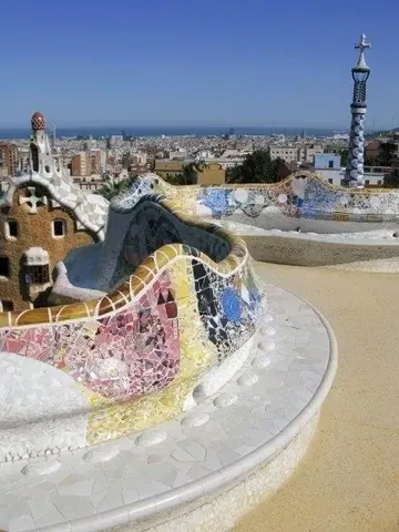 Colorful mosaic dragon sculpture with blue, pink and gold tiles overlooking Barcelona cityscape