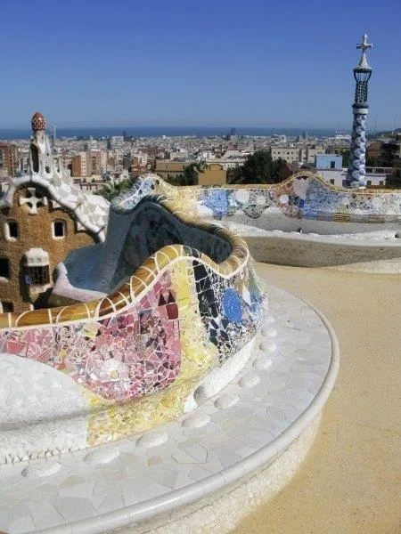 Colorful mosaic dragon sculpture with blue, pink and gold tiles overlooking Barcelona cityscape
