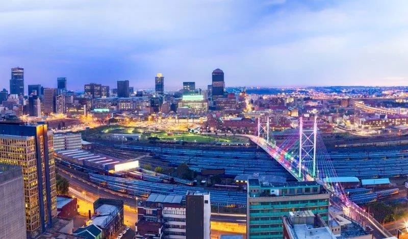 Twilight cityscape with lit skyscrapers, suspension bridge over water, and glowing downtown skyline