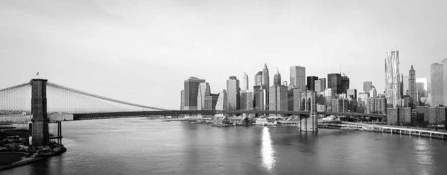 Black and white cityscape featuring Brooklyn Bridge and Manhattan skyline across water