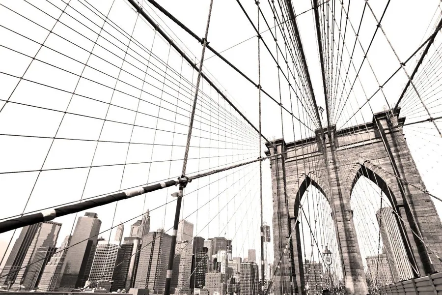 Brooklyn Bridge cables and NYC skyline viewed through architectural geometric perspective in black and white.