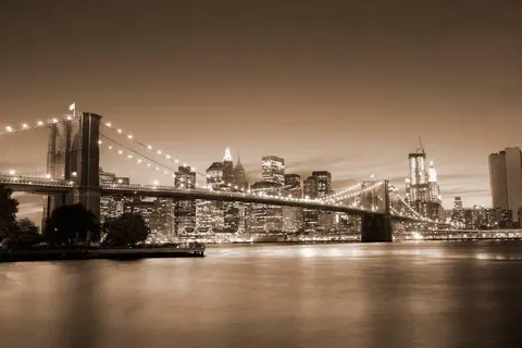 Sepia-toned New York City nightscape with illuminated Brooklyn Bridge and Manhattan skyline reflected in water