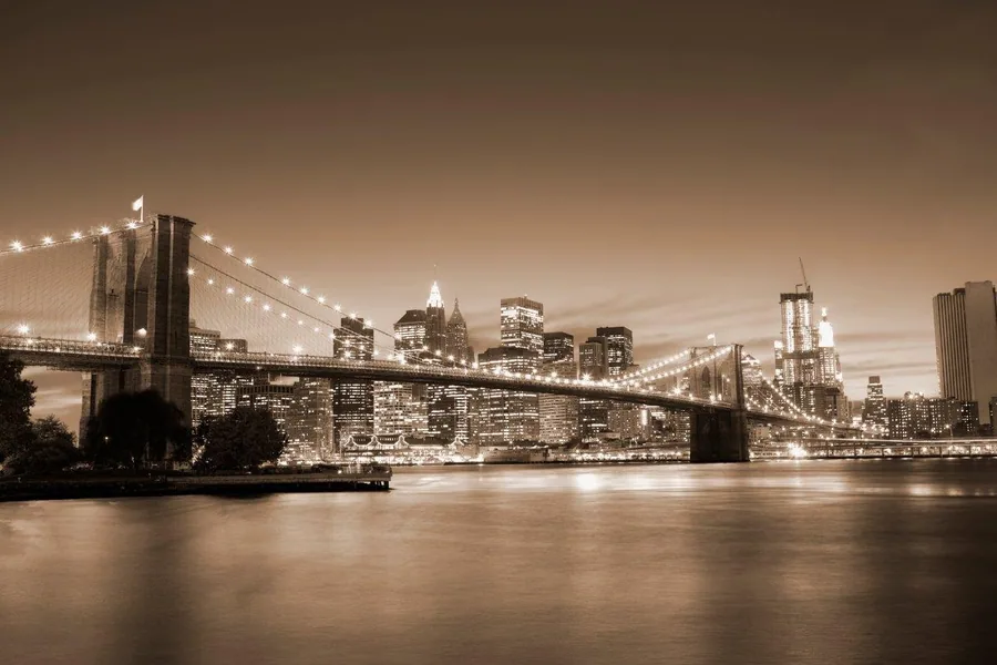 Sepia-toned New York City nightscape with illuminated Brooklyn Bridge and Manhattan skyline reflected in water