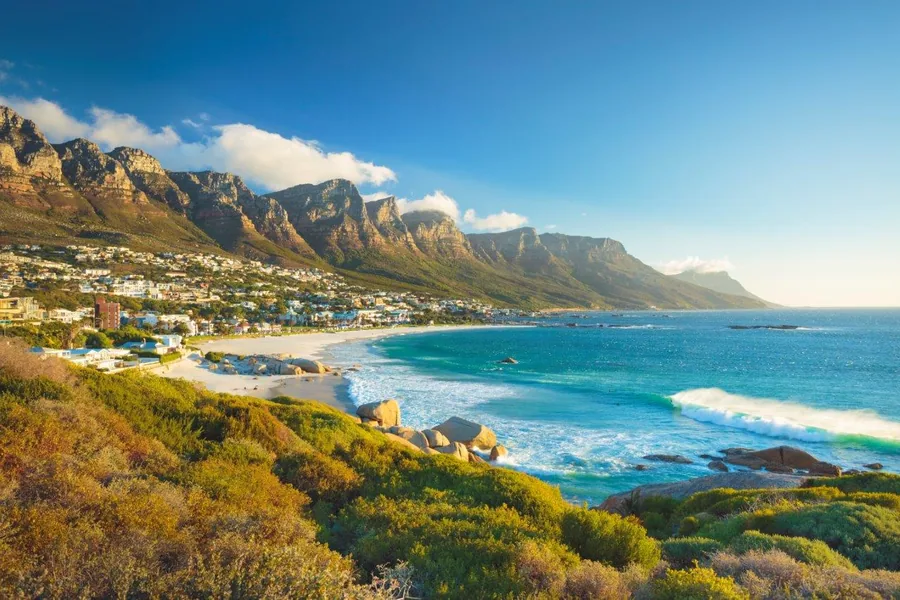 Aerial view of Camps Bay beach with turquoise ocean, white sand, and Table Mountain backdrop in South Africa.