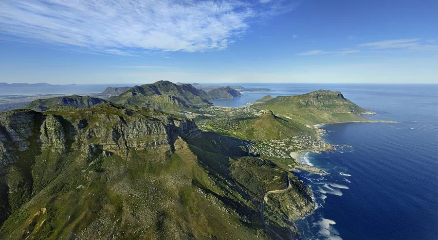 Aerial view of green mountains meeting deep blue ocean with coastal settlement below