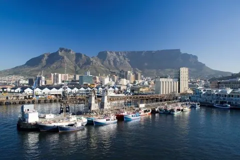 Cape Town harbor with Table Mountain, cityscape, boats, and waterfront buildings under clear blue sky