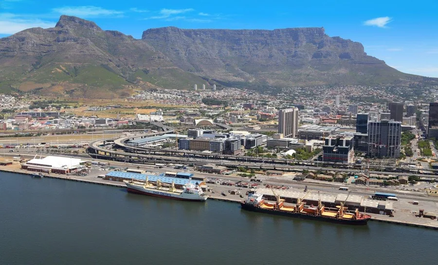 Aerial view of Cape Town city with Table Mountain, harbor, ships, and urban development under blue sky