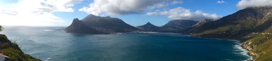 Panoramic view of Cape Town's coastline with Table Mountain, blue ocean, and dramatic cliff formations.