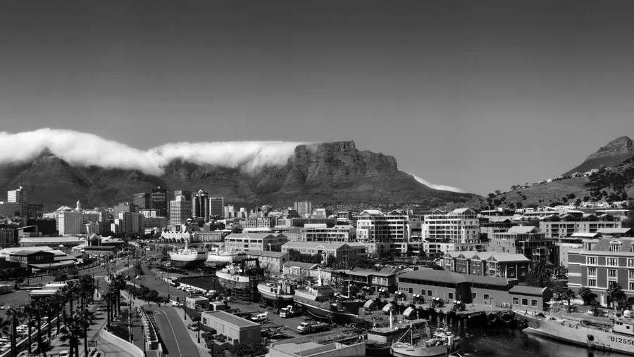 Black and white photograph of Cape Town's skyline with Table Mountain, clouds, harbor, and city buildings