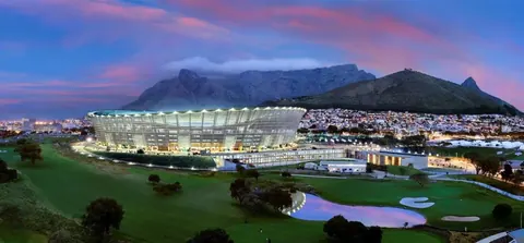 Illuminated modern stadium at dusk with Table Mountain and city lights in background under purple twilight sky