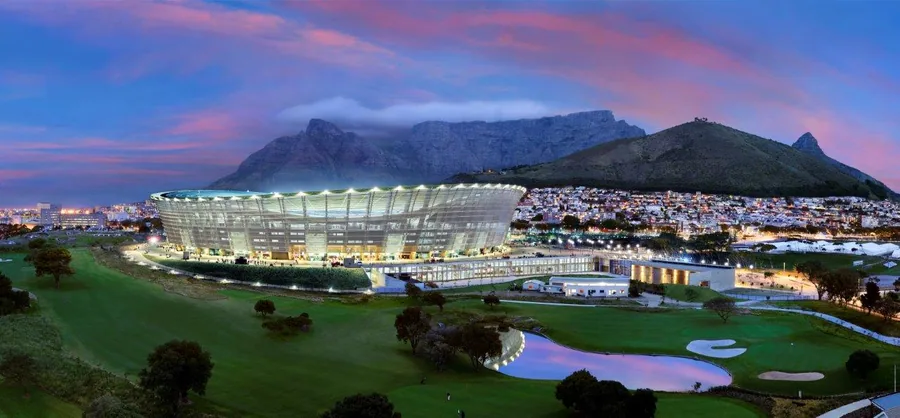 Illuminated modern stadium at dusk with Table Mountain and city lights in background under purple twilight sky
