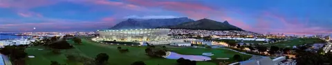 Twilight panorama of Cape Town with illuminated stadium, mountains, and city lights reflecting on water