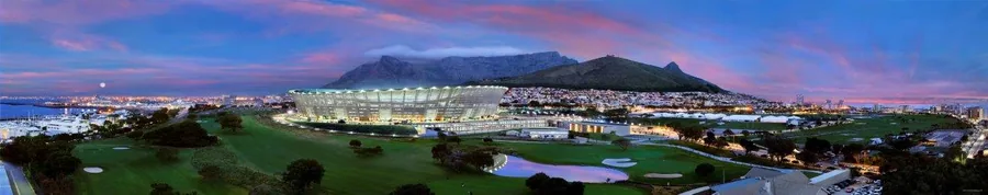 Twilight panorama of Cape Town with illuminated stadium, mountains, and city lights reflecting on water