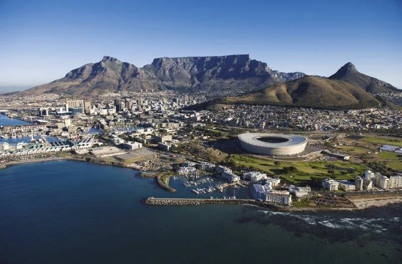Aerial photograph of Cape Town showing Table Mountain, city skyline, waterfront, and stadium.