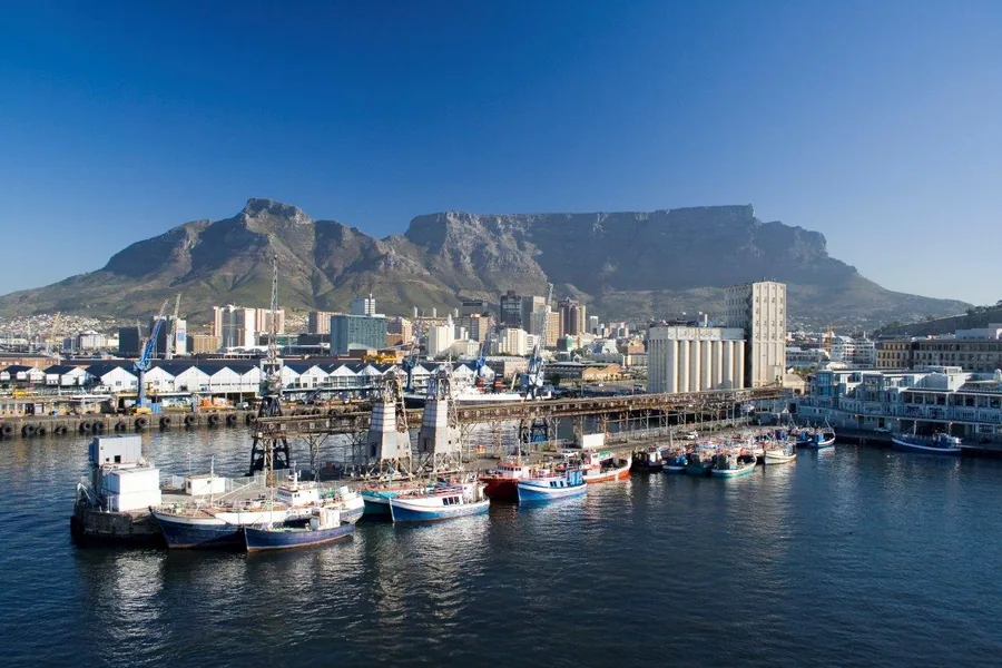 Cape Town harbor with Table Mountain, colorful fishing boats, and city skyline under blue sky